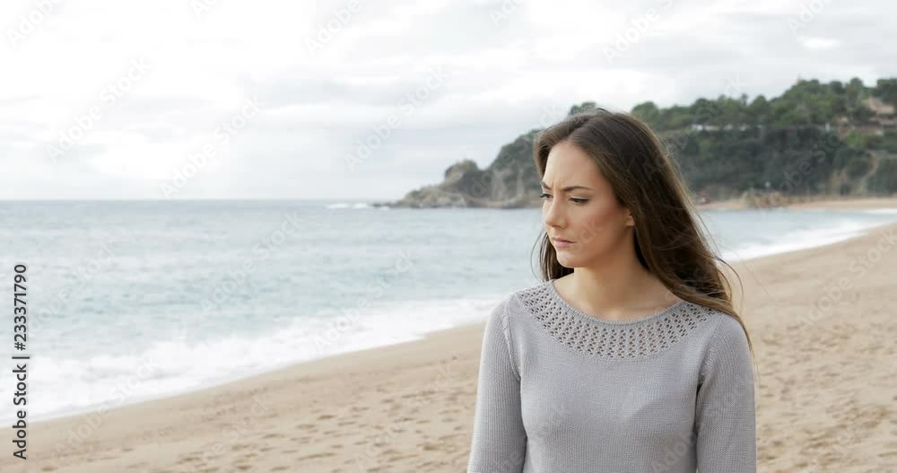 Worried woman walking alone on the beach looking at ocean Worried woman walking alone on the beach looking at ocean