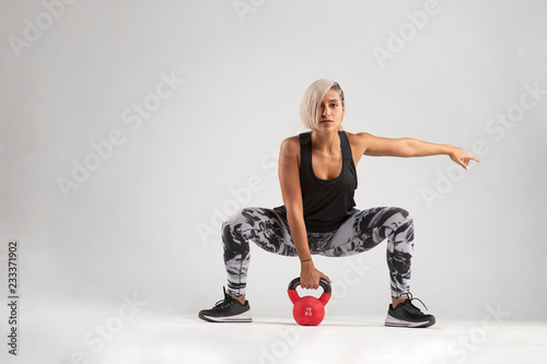 Beautiful female Middle Eastern fitness athlete with modern funky hairstyle and wearing sports clothing about to do a kettle bell lifting exercise from a squatting position