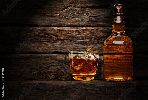 Photographie Bottle and glass of whiskey on wooden table or desk background