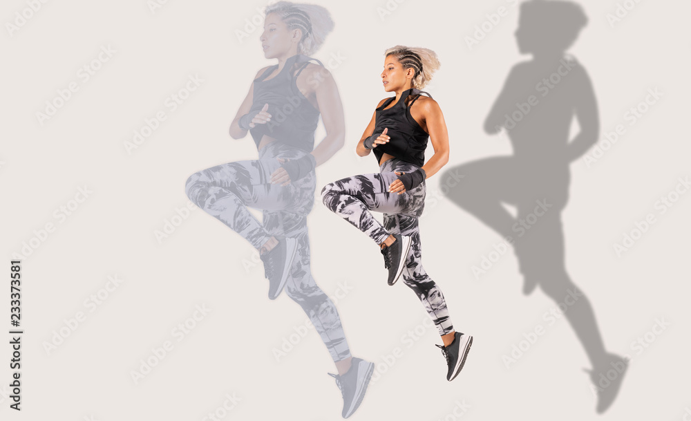 Obraz premium Composite of .a beautiful female Middle Eastern fitness athlete with modern funky hairstyle and wearing sports clothing doing a dramatic leap with a shadow and larger reflection on background 