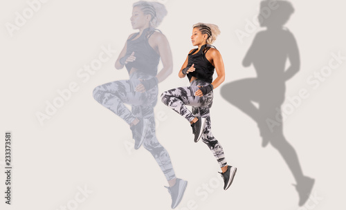 Composite of .a beautiful female Middle Eastern fitness athlete with modern funky hairstyle and wearing sports clothing doing a dramatic leap with a shadow and larger reflection on background 