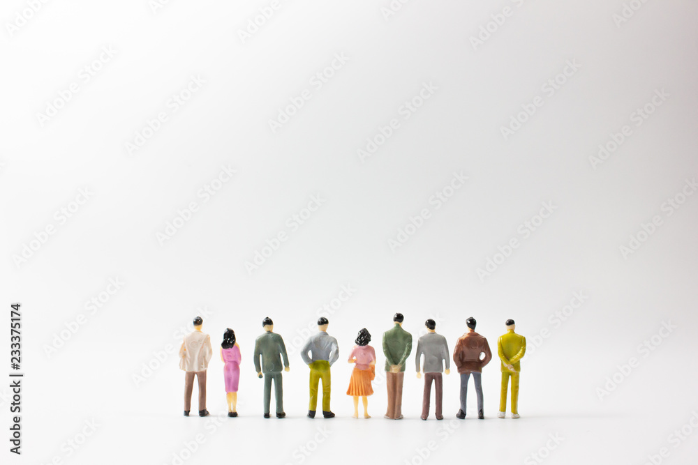 A group of miniature business people stand on white background back view.