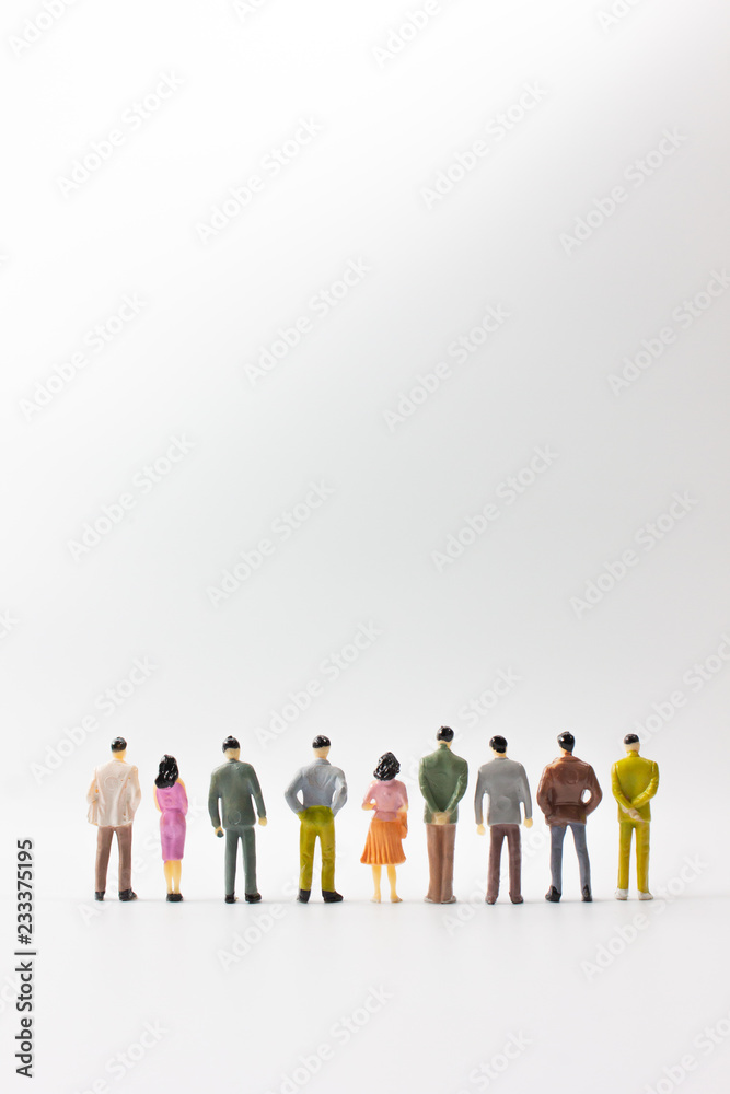 A group of miniature business people stand on white background back view verticle.