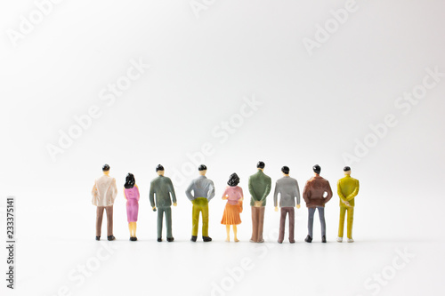 A group of miniature business people stand on white background back view.