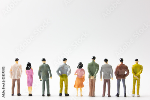 A group of miniature business people stand on white background back view.