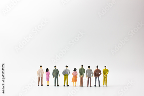 A group of miniature business people stand on white background back view.