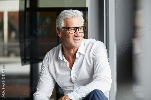 Smiling mature businessman wearing eyeglasses looking through window photo