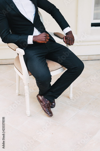 black man in a business suit sitting in a chair, wedding concept. groom black leather. white shirt black suit