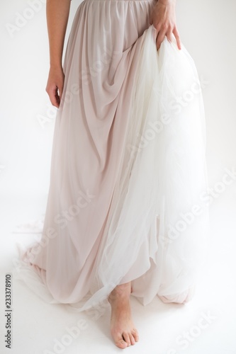 Bride in an elegant silk dress stands and holds the dress by the edge belt, White background