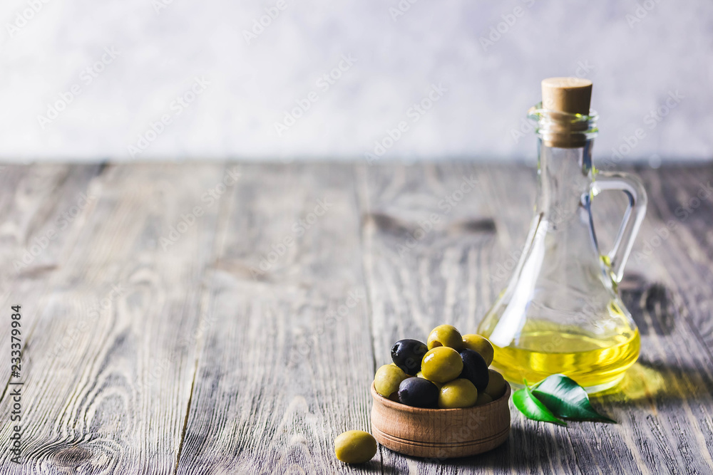 Obraz premium Extra vergin olive oil in glass jar, marinated olives in wooden bowl on rustic background. Selective focus, space for text.