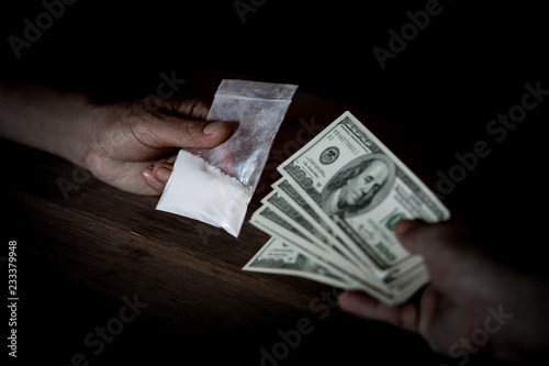 Hand of addict man with money buying dose of cocaine or heroine or another narcotic from drug dealer. Drug abuse and traffic concept.