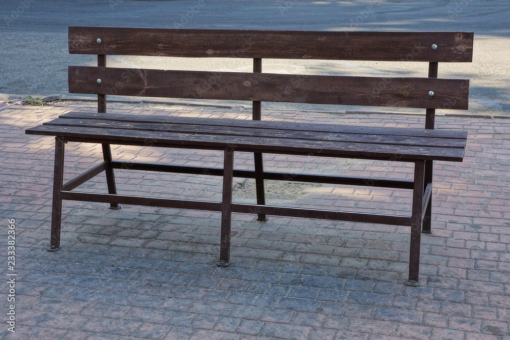 one brown wooden bench stands on a gray sidewalk outside