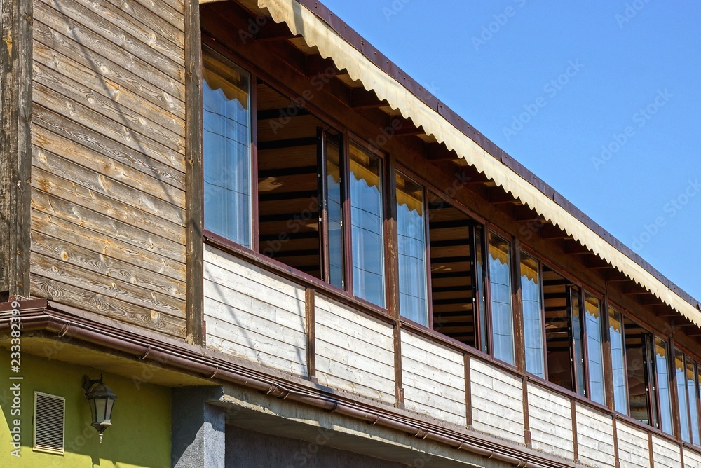 large wooden brown balcony porch with windows against a blue sky