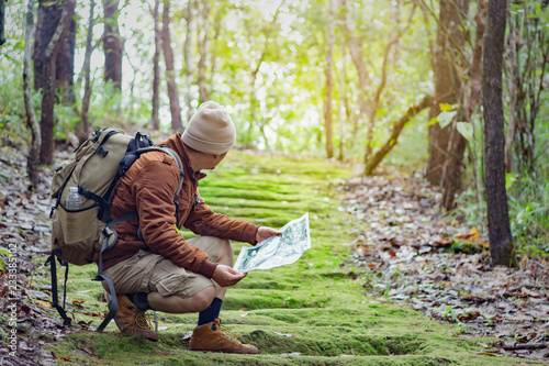 Man sits on a moss covered forest and looks for a route on the map.