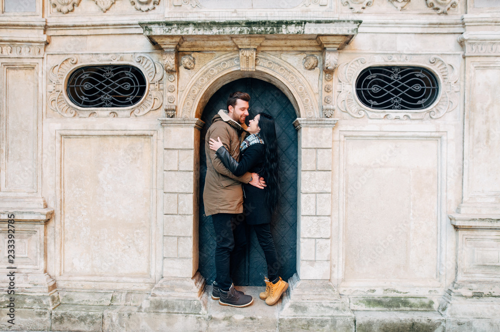 Beautiful young brunette couple stand in the arch in the doors of an old building