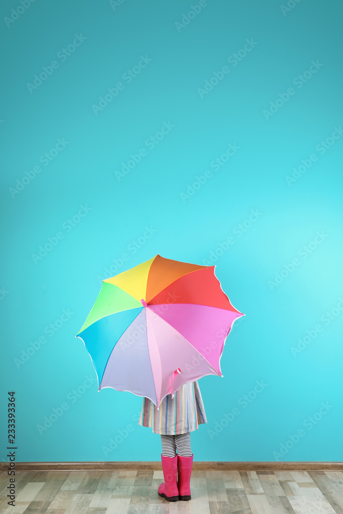 Little girl with rainbow umbrella near color wall. Space for text