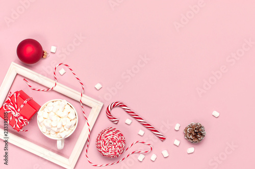 White mug with marshmallows Candy Cane gifts boxes red ball packaging lace photo frame on pink background top view Flat Lay. Winter traditional drink food Festive celebration Christmas New Year