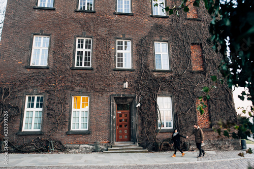 A couple walks near a building with many windows