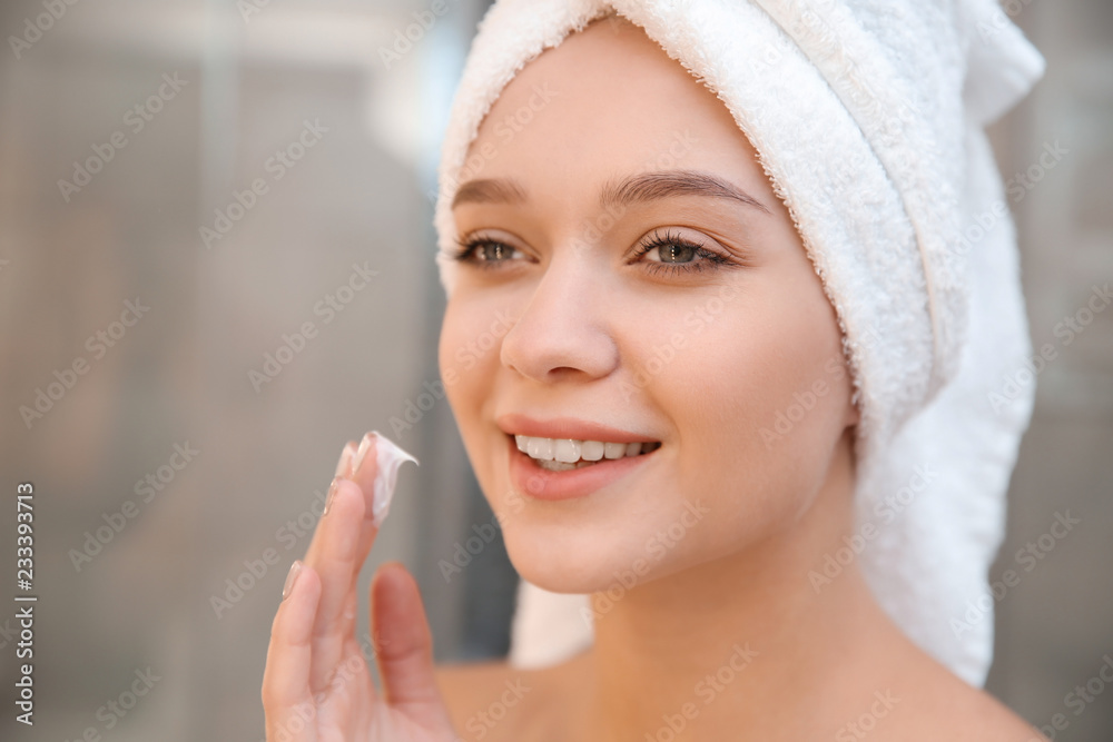 Beautiful woman with towel on head applying face cream in bathroom Beautiful woman with towel on head applying face cream in bathroom