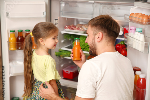 Young father with daughter taking juice from refrigerator at home