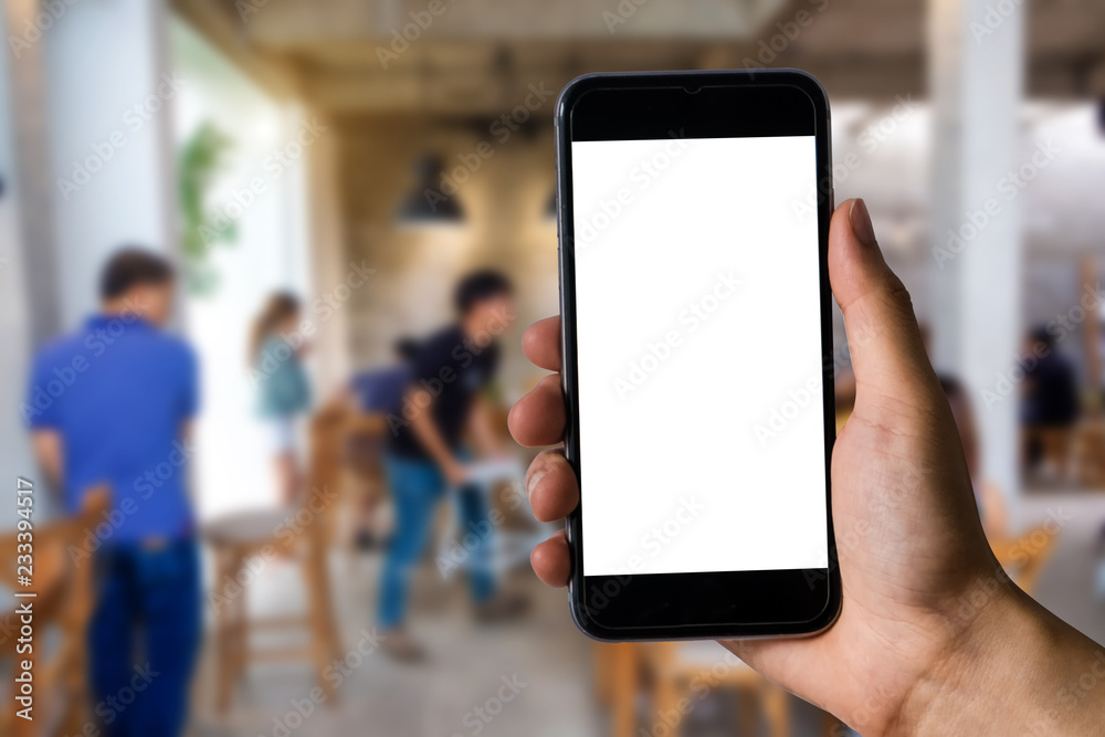 Mockup image of hand holding white mobile phone with blank white screen in cafe.