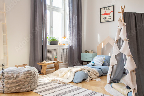 Pouf and tent in scandinavian bedroom interior with drapes at window and poster above bed. Real photo
