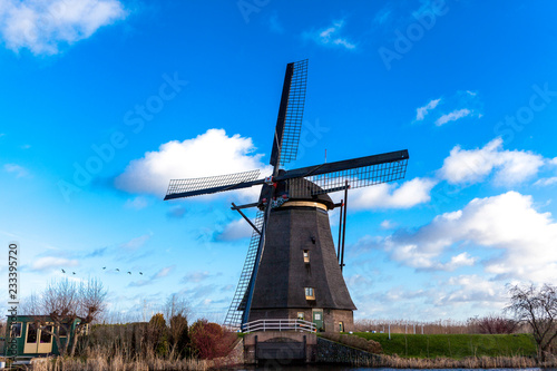 Traditional dutch windmill near the canal. Netherlands. Old windmill stands on the banks of the canal, and water pumps. White clouds on a blue sky, the wind is blowing.
