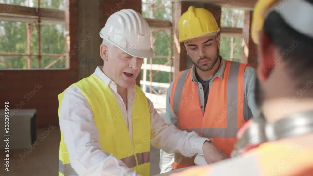 People working in construction site. Men at work in new house inside apartment building. Team of workers at work talking with engineer and looking at blueprint during business meeting