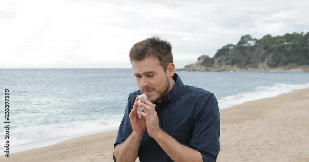 Allergic man sneezing covering mouth with a wipe walking on the beach Allergic man sneezing covering mouth with a wipe walking on the beach