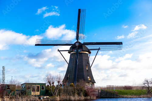 Traditional dutch windmill near the canal. Netherlands. Old windmill stands on the banks of the canal, and water pumps. White clouds on a blue sky, the wind is blowing.