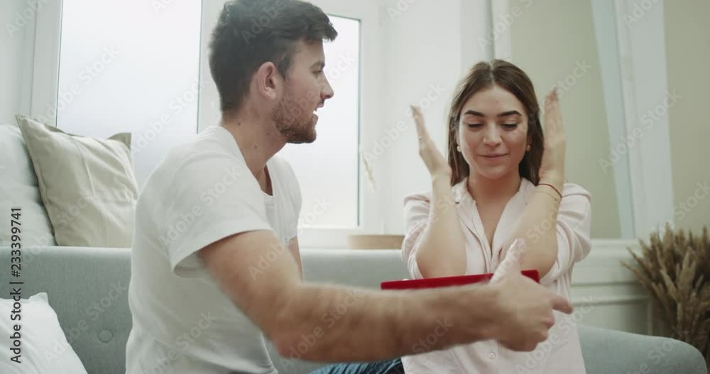 Beautiful young couple home atmosphere , sitting on the sofa , man giving the present for his woman closeup she is very happy for the surprise. Beautiful young couple home atmosphere , sitting on the sofa , man giving the present for his woman closeup she is very happy for the surprise.