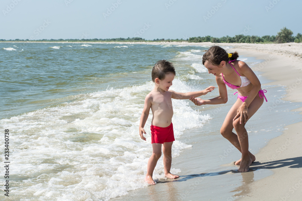 Older sister gives hand to younger little brother on the seashore Older sister gives hand to younger little brother on the seashore