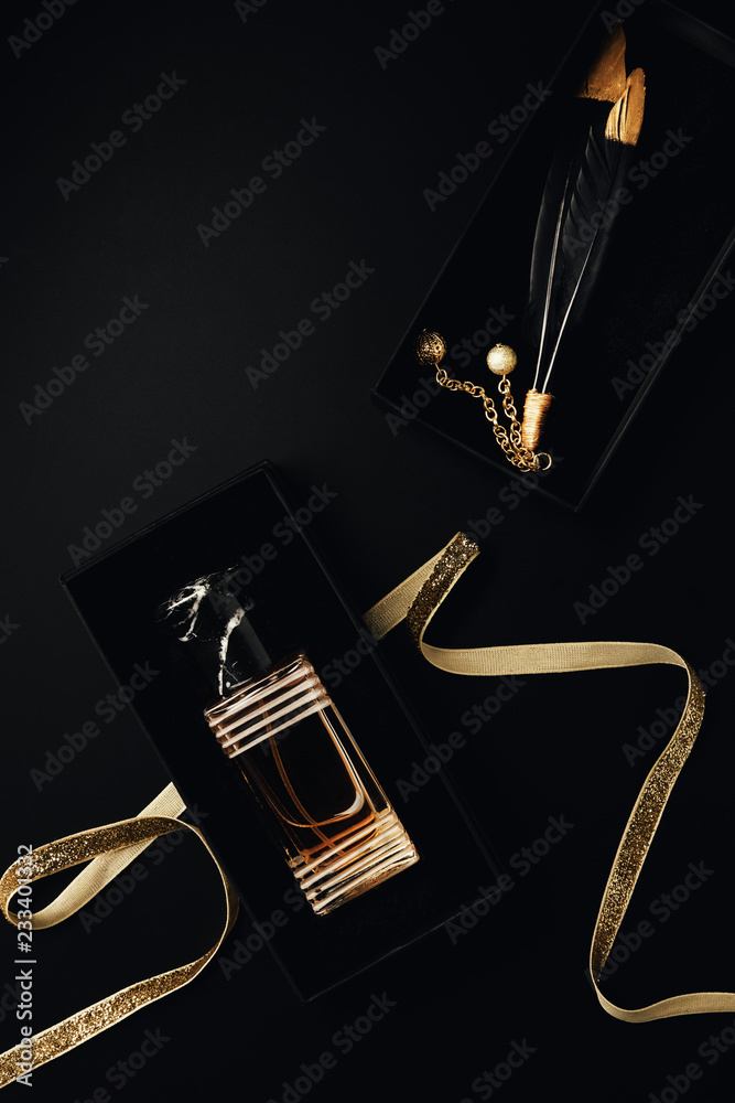 top view of perfume bottle with golden ribbon, gift box and decorative feathers on black