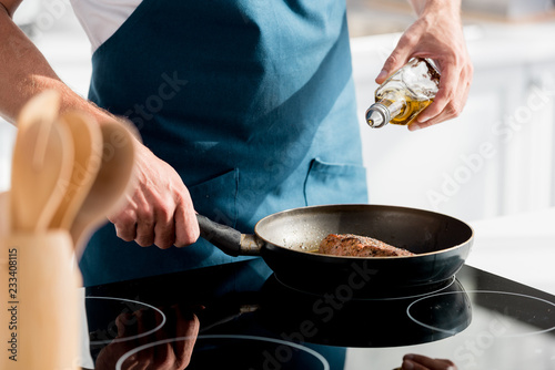 partial view of man pouring oil on steak