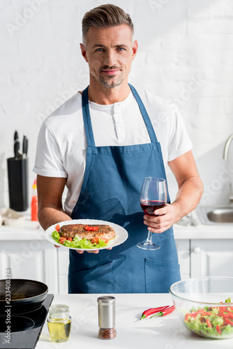 handsome man with cooked meat in one hand and glass of wine in other