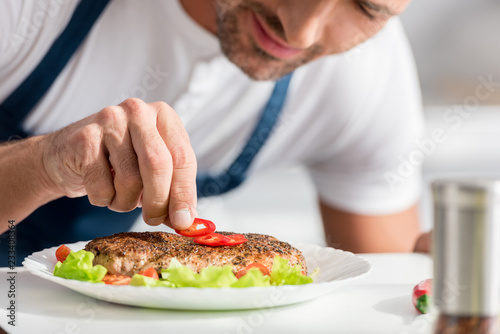 Fototapeta Naklejka Na Ścianę i Meble -  close up view of adult man adding peper to cooked steak