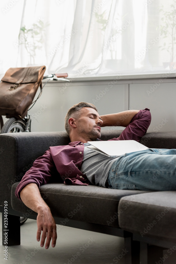 man laying on sofa with laptop and sleeping at home office