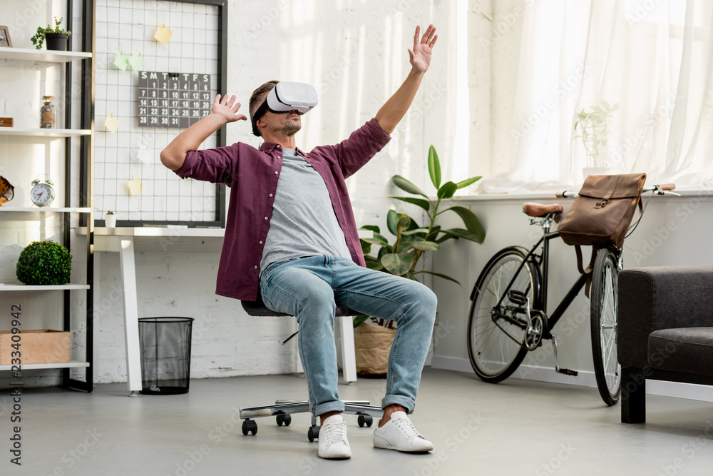 man sitting on chair and gesturing in virtual reality headset at home office