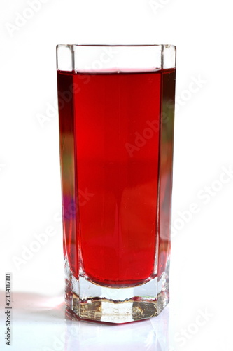 glass with berry red ruby juice on white background with reflection on glass table