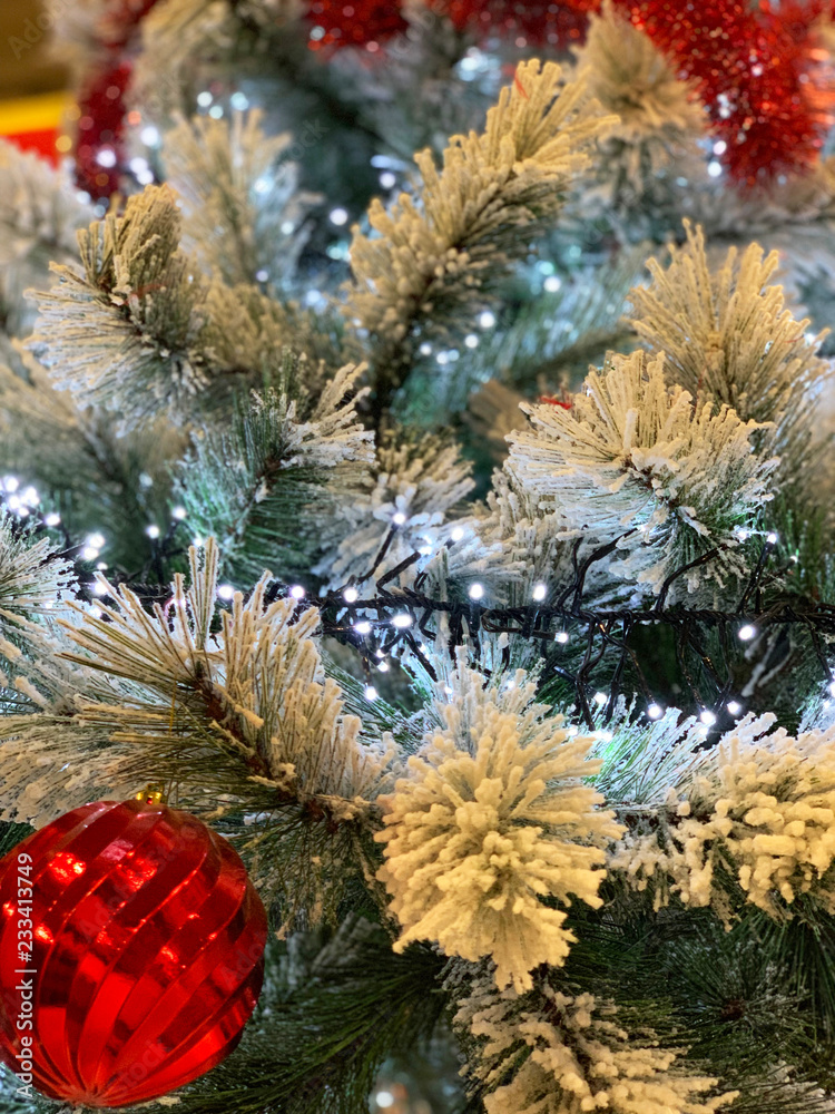 Close-up on Christmas tree covered with snow decorated with red glittering balls and glowing lights