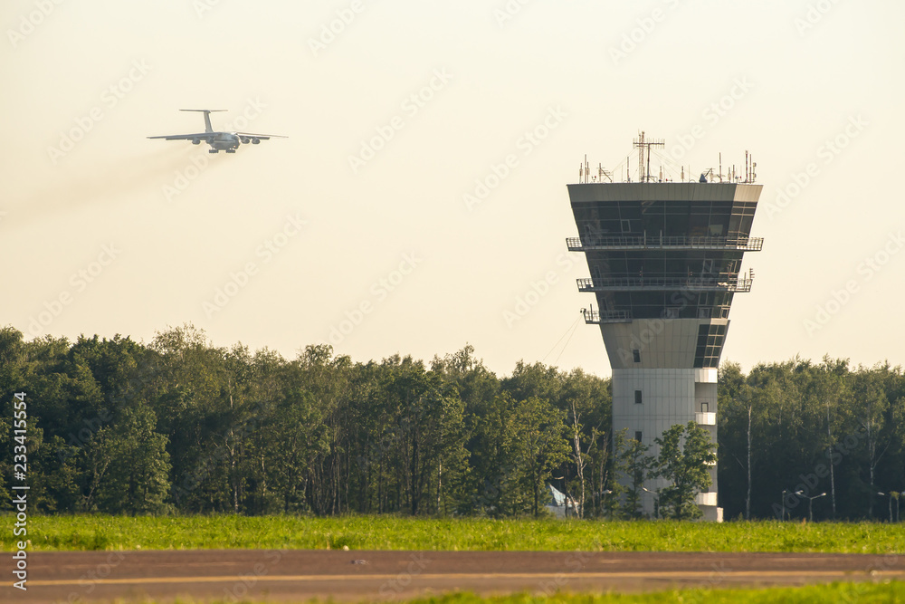Fototapeta premium Airport control tower and commercial airplane landing at sunset