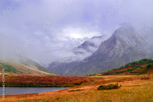 misty mountain valley with lush autumn vegetation and small lake  sheltered by low clouds