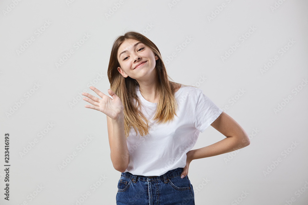 Friendly girl dressed in a white t-shirt and jeans shows hi on a white background in the studio Friendly girl dressed in a white t-shirt and jeans shows hi on a white background in the studio