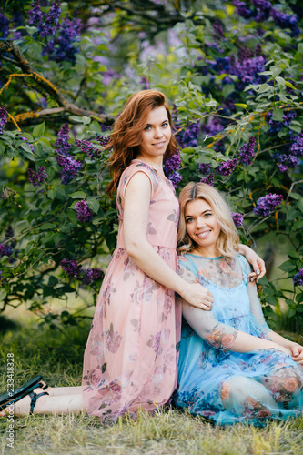 Fashion portrait of happy twin sisters. Stylish young beautiful twins. Fabulous female relatives childhood memories.  Lovely funny women couple playing and fooling. Pair of girls in dresses outdoor.