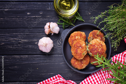 Homemade cutlets with herb and spices on black wooden background.