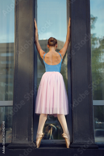 Ballet dancer dancing on street. Young ballerina in pink tutu. Ballet feet on the point. Pretty ballerina near the theater doing exercise.