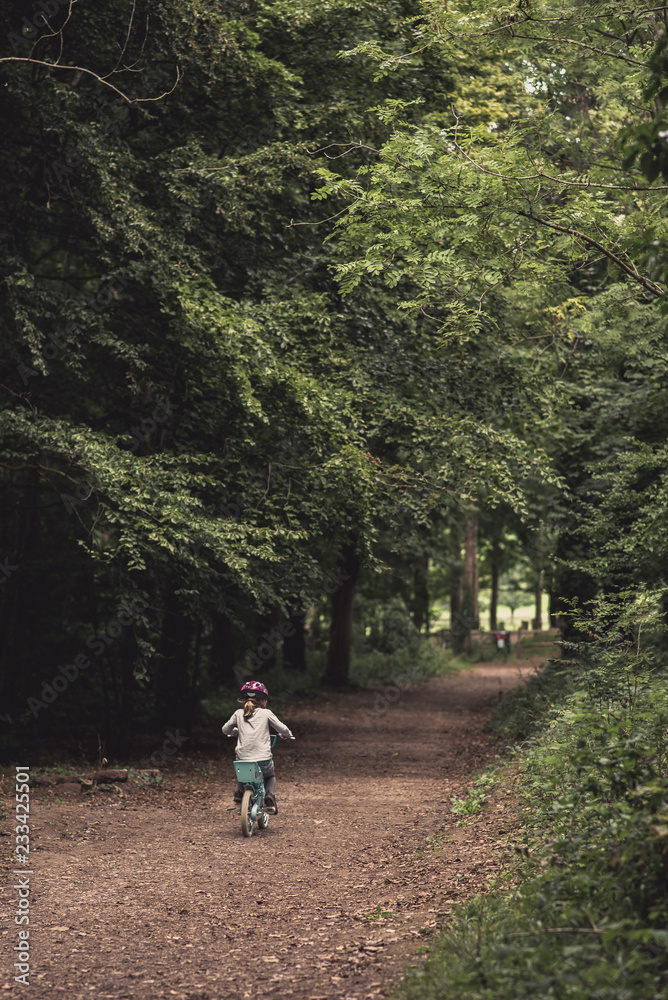 Fototapeta premium Young girl riding bike through woodland