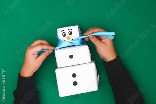 The original design of the three Christmas gift of white paper, a satin ribbon in the form of a snowman on a green background. Step by step on the photo. Handmade, DIY. Snowman from gifts.