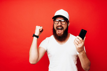 Man holding smartphone over red background and celebrating
