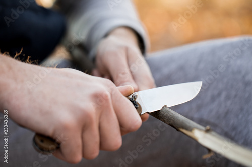 Close-up of the tourist's hands, sharpening a stick with a knife. The concept of travel, extreme and survival